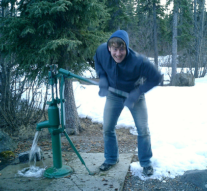 Young man pumping a hand water pump.